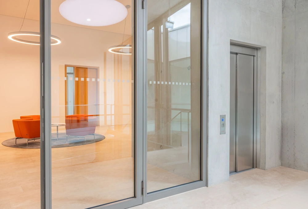 Modernes Foyer mit orangefarbenen Sesseln, Glastüren und einem Aufzug