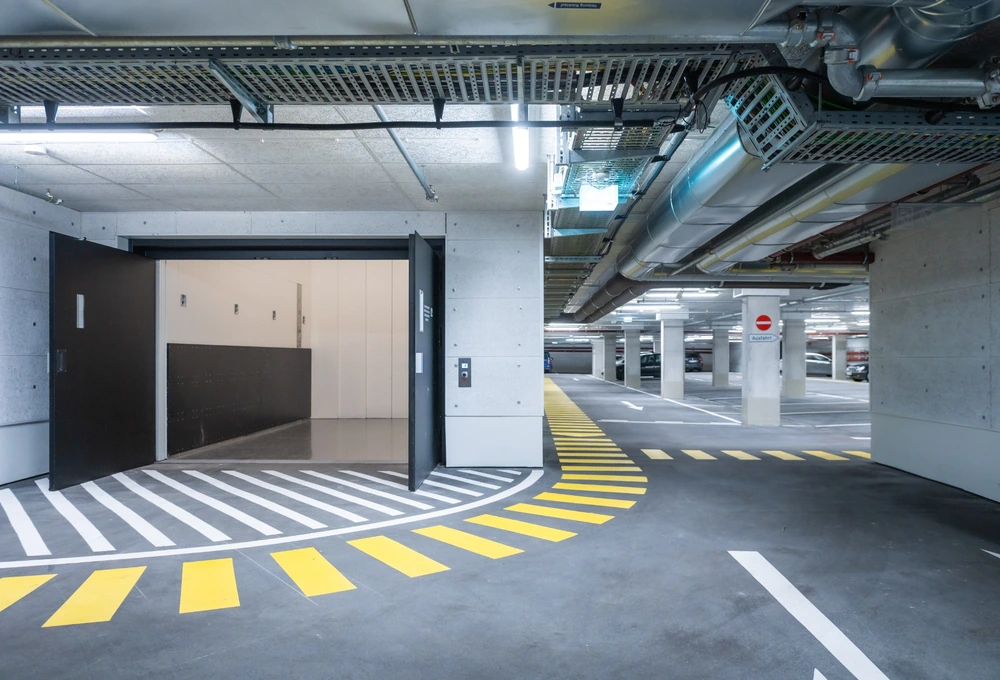 Geöffnete Aufzugstüren in einer Tiefgarage mit gelb-weißen Bodenmarkierungen