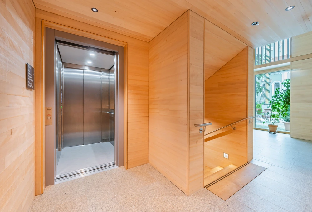 Holzverkleideter Eingangsbereich mit offenem Aufzug und Treppe