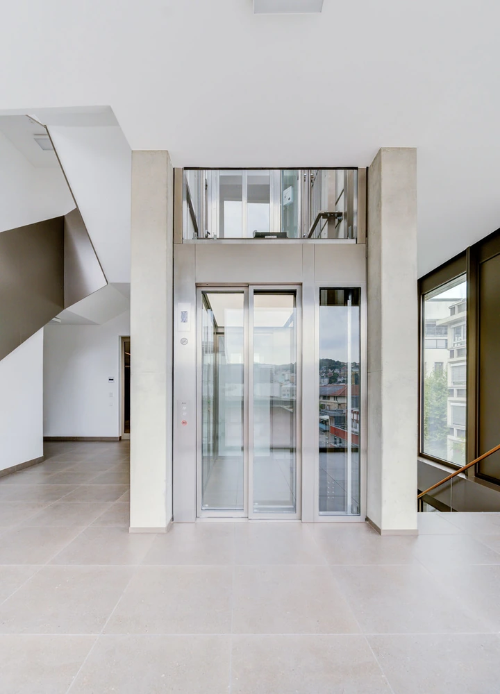 Heller Eingangsbereich eines modernen Gebäudes mit gläsernem Aufzug und Treppe