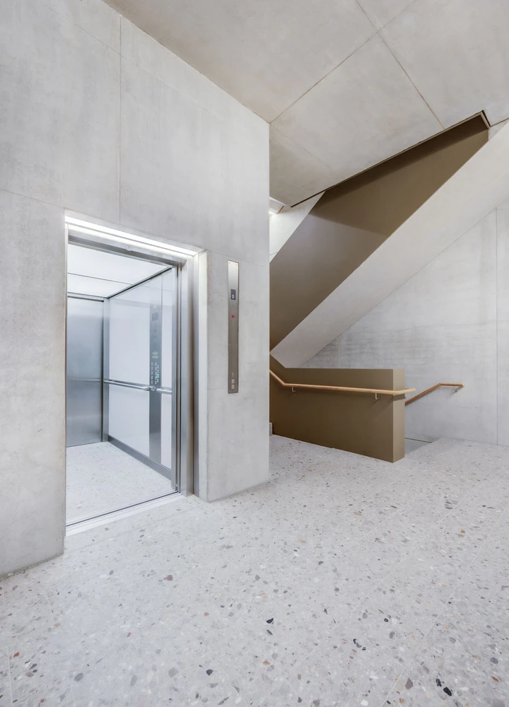 Offener Aufzug neben einer Betontreppe in einem modernen, hellen Gebäude