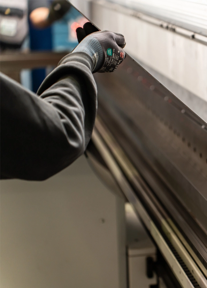 Behandschuhte Hand führt ein Metallblech in eine industrielle Maschine