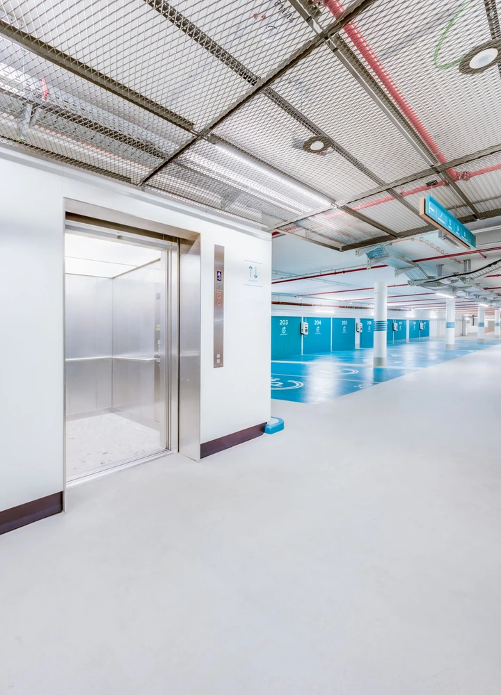 Geöffneter Aufzug in einem hellen Parkhaus mit blau markierten Stellplätzen