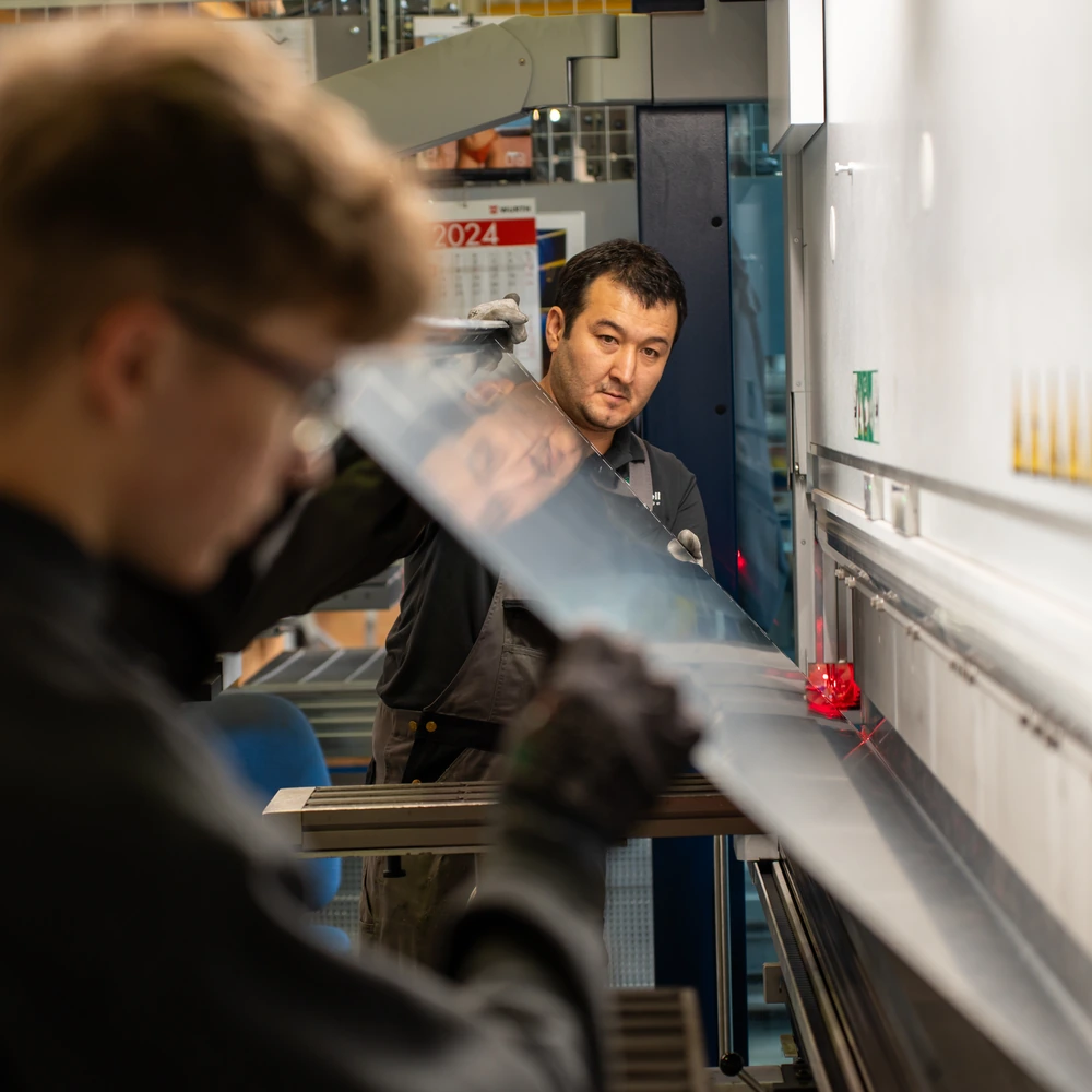 Zwei Mitarbeiter bearbeiten gemeinsam ein großes Blech an einer Industriemaschine