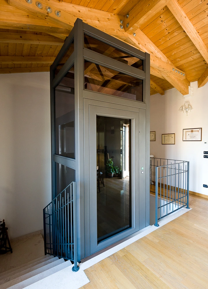 Verglaster Aufzug in einem Innenraum mit Holzdecke und Treppenhaus