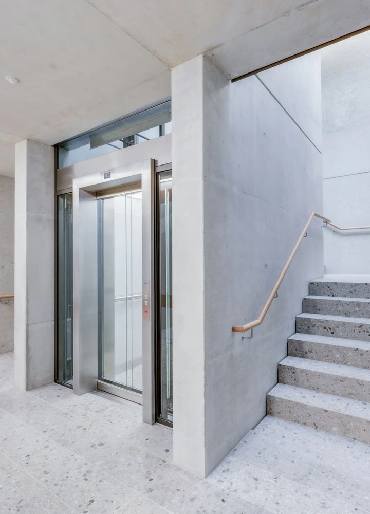 Aufzug neben einer Betontreppe in einem hellen, modernen Gebäude