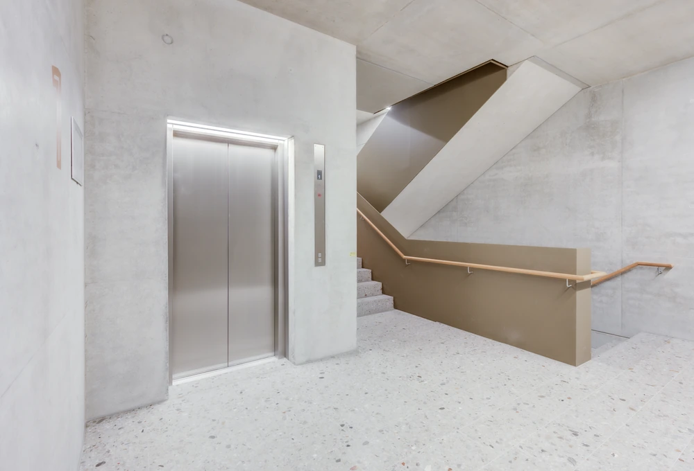 Betonierter Flur mit geschlossenem Aufzug und angrenzender Treppe