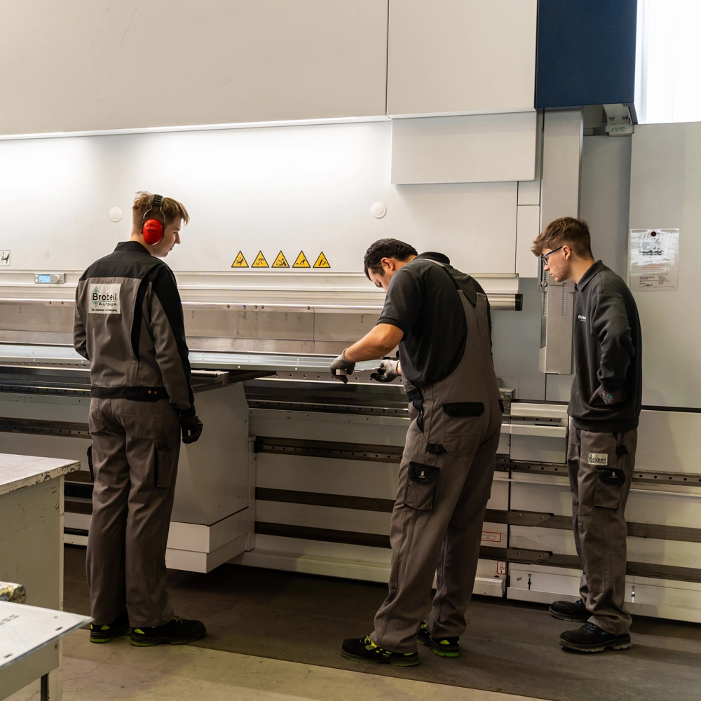 Drei Mitarbeitende bedienen und überwachen gemeinsam eine industrielle Abkantpresse