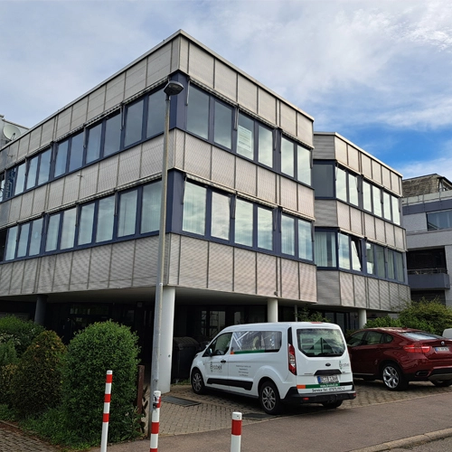 Dreistöckiges Bürogebäude mit großen Fenstern und geparkten Fahrzeugen vor dem Eingang