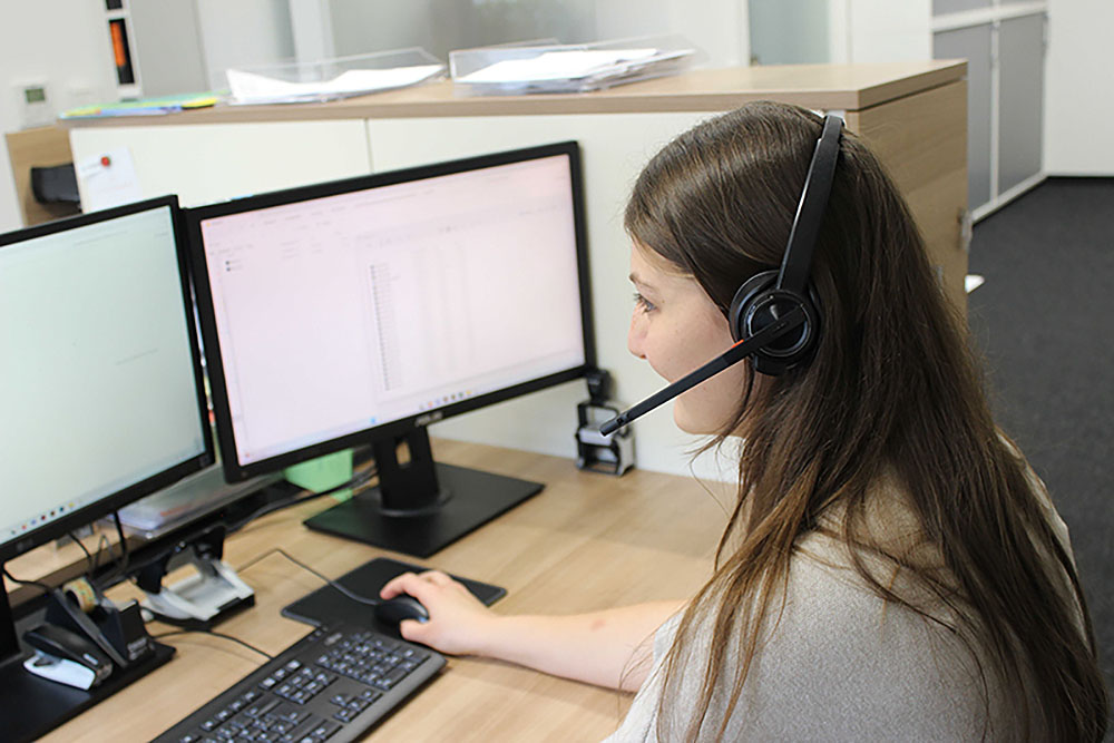 Mitarbeiterin mit Headset arbeitet an zwei Computermonitoren