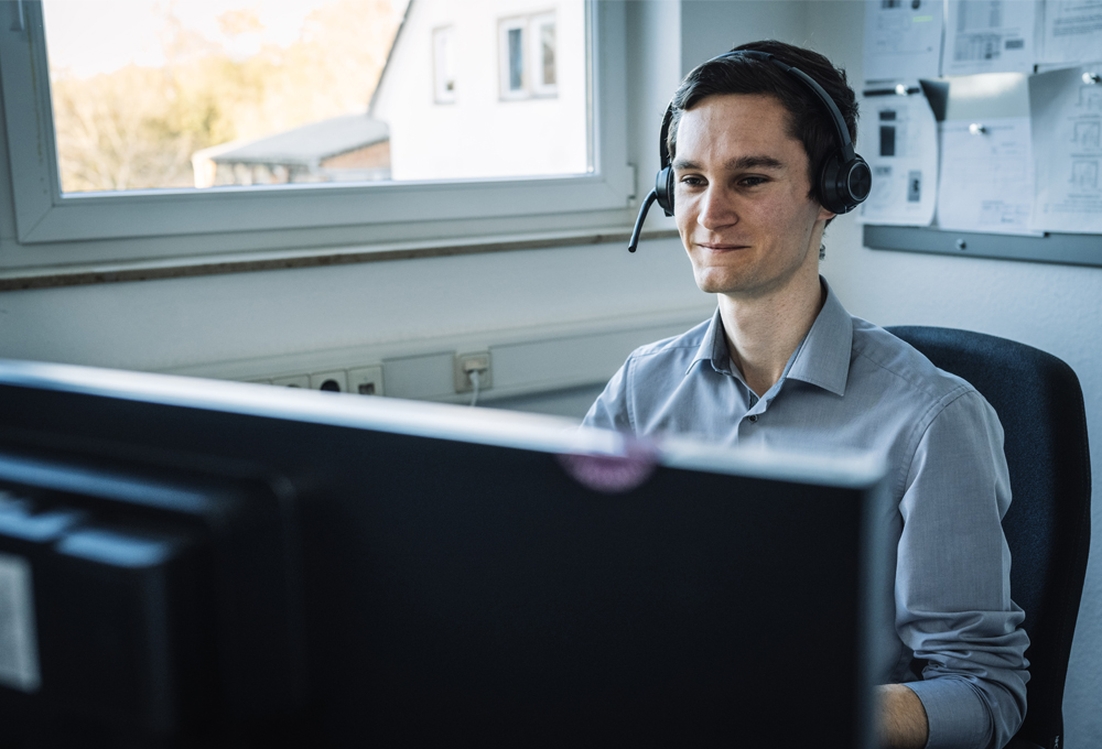 Mann mit Headset sitzt vor einem Computerbildschirm im Büro